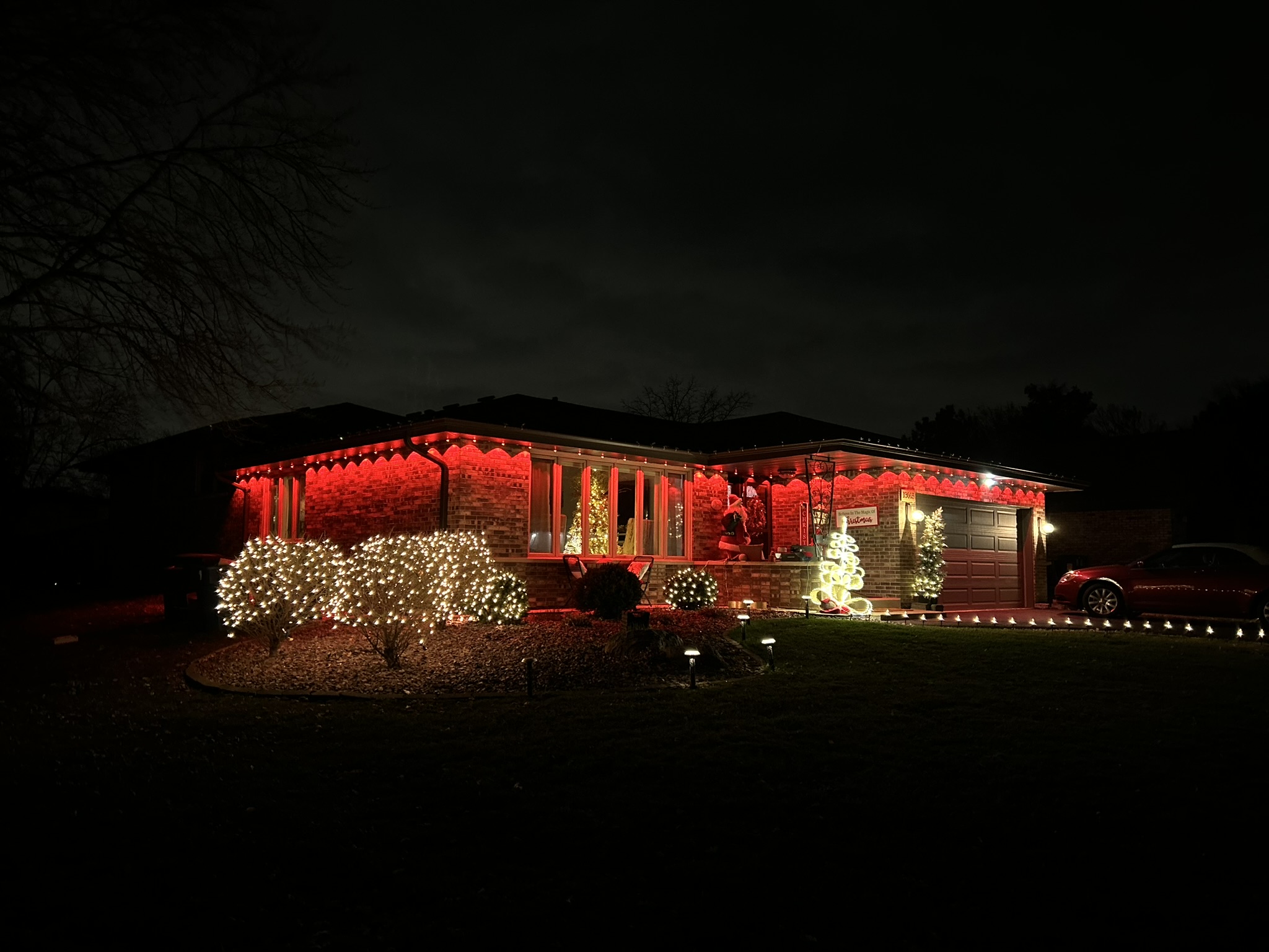 Home lit in deep red roofline lighting with warm white bushes below